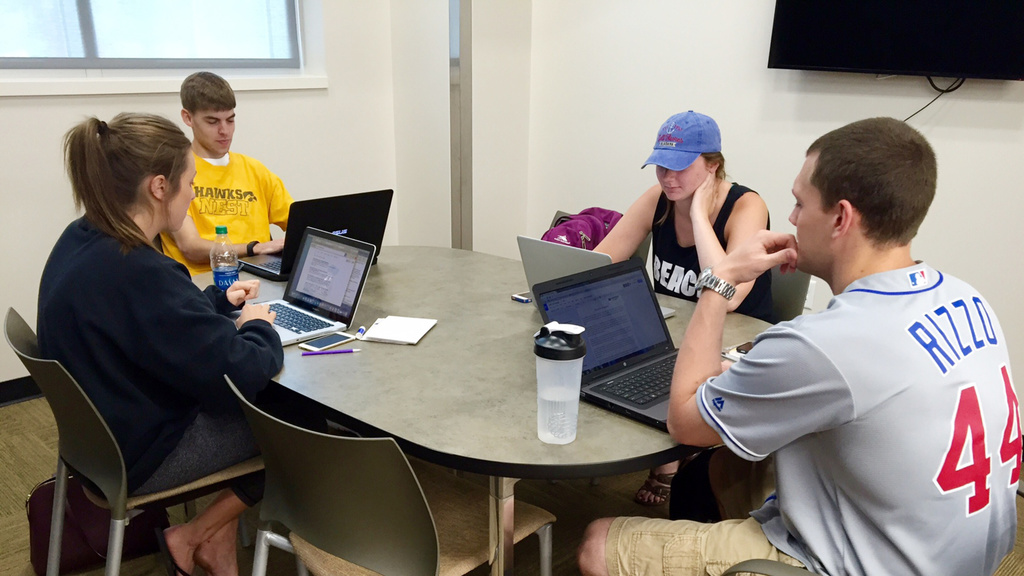 students in sporting clothing at desk with laptops